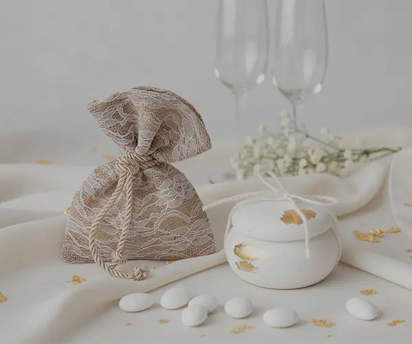 Mărturii de nuntă elegante, săculeț din dantelă și cutiuță albă aurie pe masă festivă
