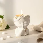 Mărturie botez lumânare parfumată fetiță albă cu degetul la gură (shh) și coroniță de flori cu detalii aurii
