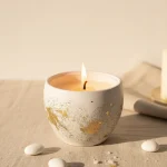 Mărturie lumânare recipient ceramic alb cu capac și decorațiuni în foiță aurie, alături de bomboane albe, ideală pentru nuntă sau botez