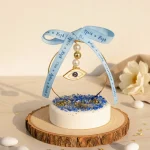marturie simbol ochi protectie pe baza rotunda alba cu pietricele decorative albastre si auriu si fundita bleu