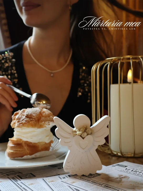 arturii deosebite sub forma de inger ceramic alb cu flori uscate, asezate ca decor pe o masa eleganta de eveniment langa un desert si o lumanare in colivie aurie, cu logo Marturia Mea vizibil.