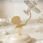 Marturii botez baiat avion sub forma unei figurine aurii cu baietel si avion decorat cu nori pe suport tip pietricica.